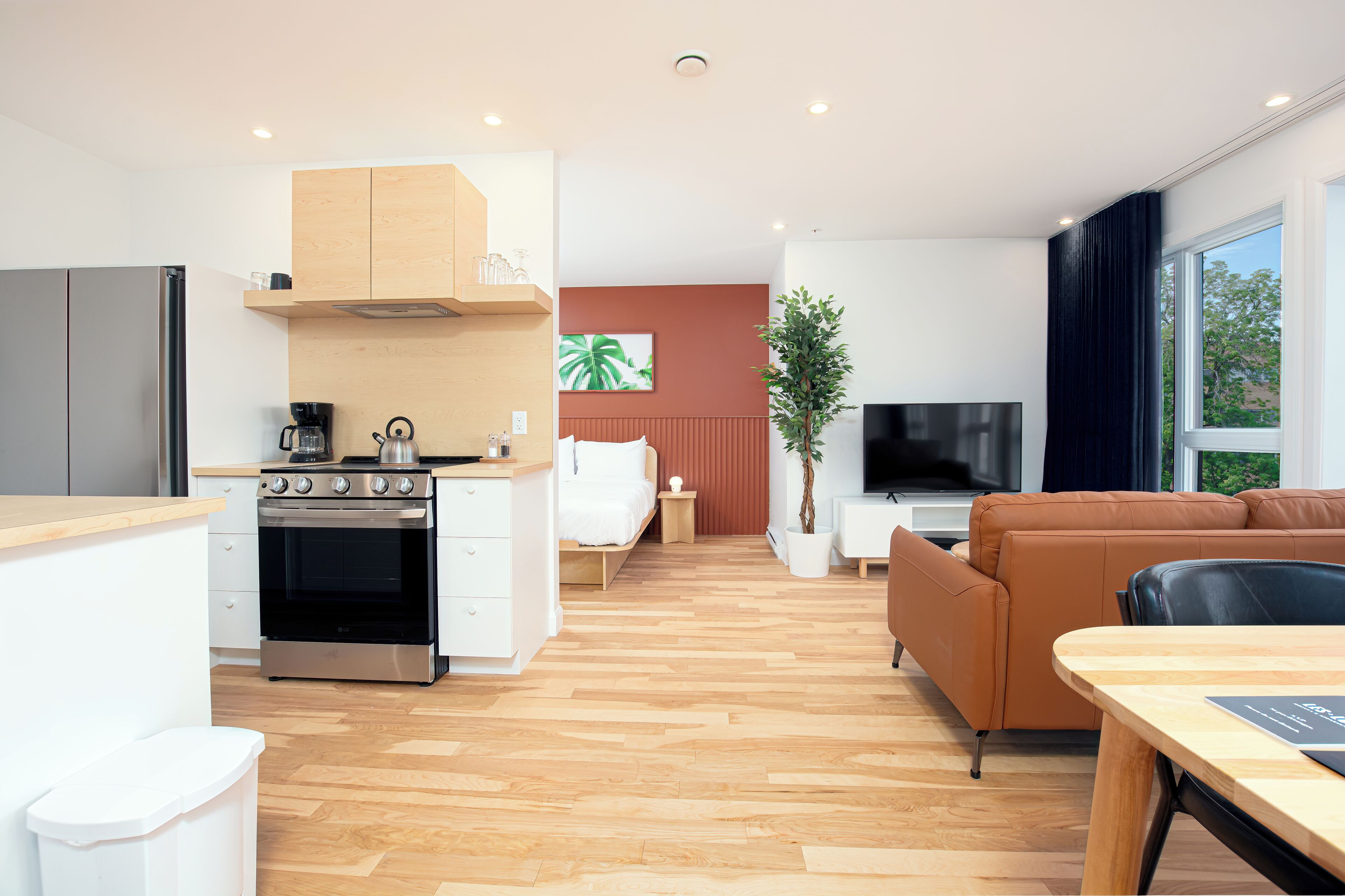 Una cocina moderna con horno empotrado, un comedor con mesa de madera, un sofá y un televisor en la sala.