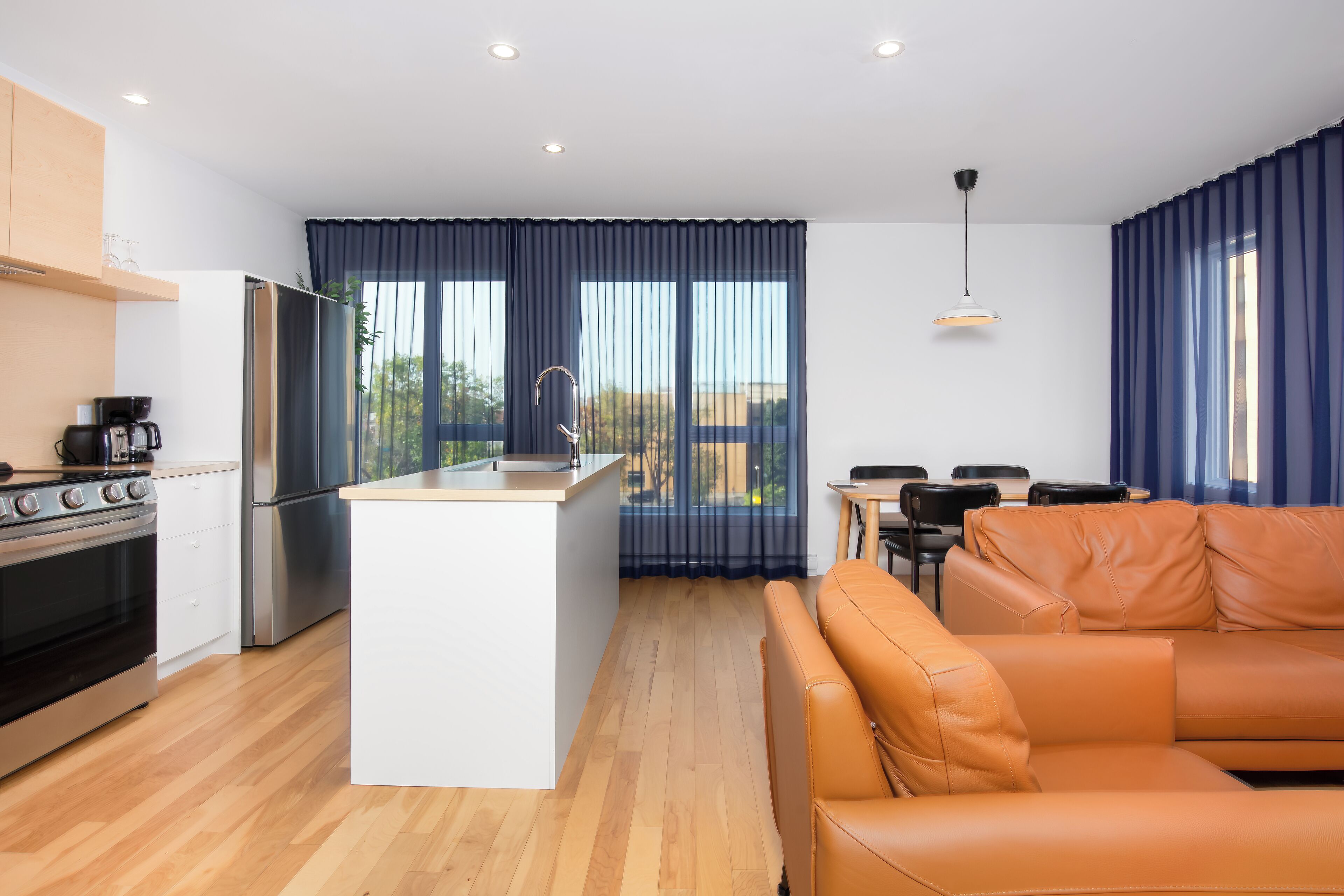 Uma cozinha moderna com uma ilha central, uma sala de jantar com mesa e cadeiras, e uma sala de estar com sofá.