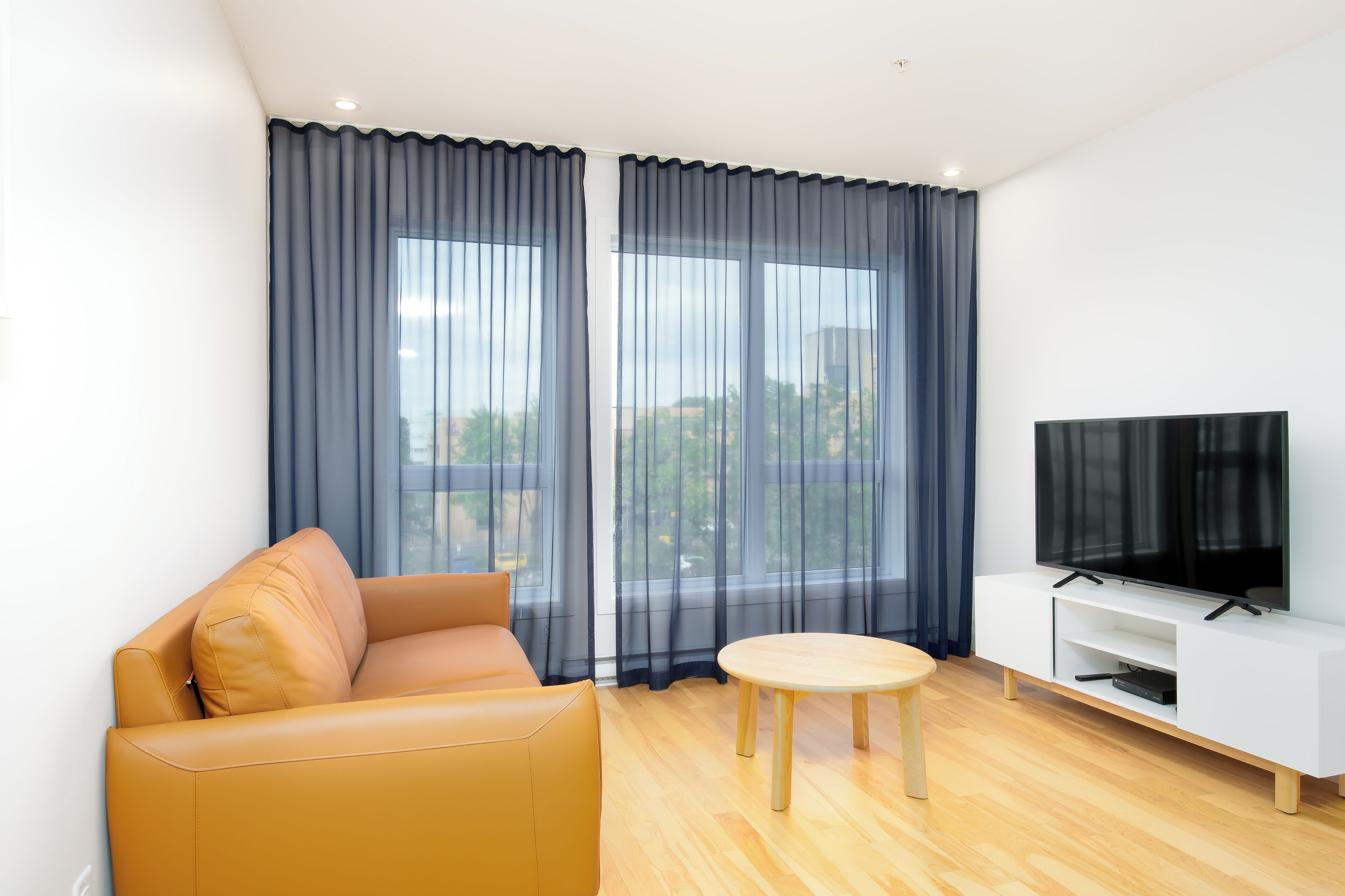 A modern living room with a sofa, a round table, and a TV on a white stand.