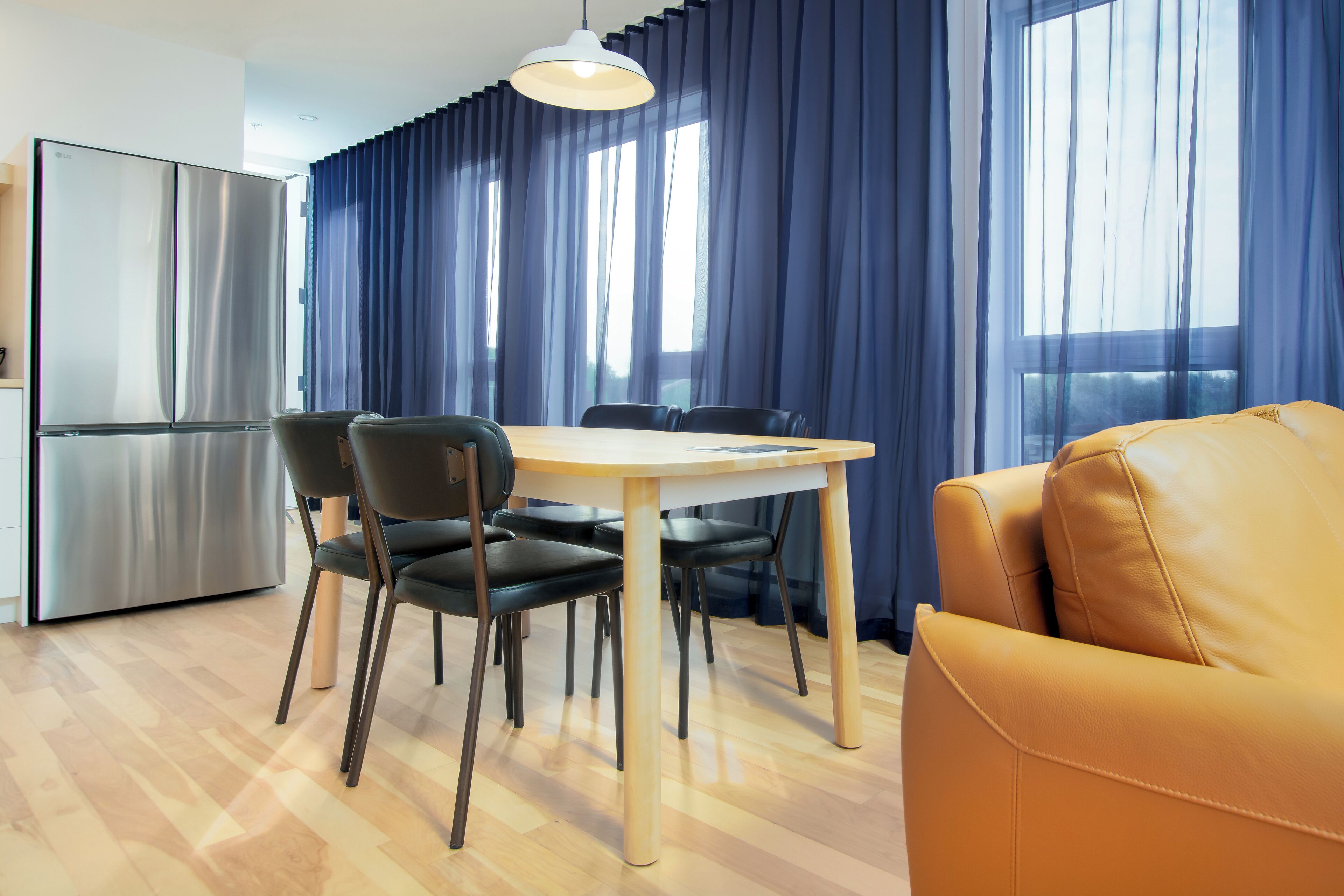 Une cuisine moderne avec un réfrigérateur en acier inoxydable, une table à manger avec quatre chaises et un canapé jaune.