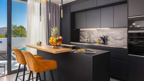 A modern kitchen with a central island, black cabinetry, and a marble backsplash. - Luxury Villa Lux with Heated Pool (Kaštel Kambelovac)