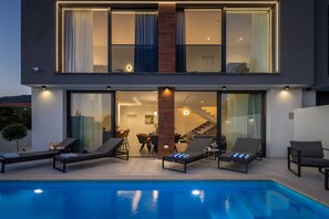 Une maison moderne à deux étages, dotée d’une piscine, d’un espace salon extérieur et d’un escalier menant à l’étage supérieur.