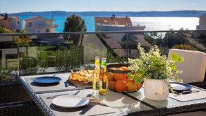 A table set on a balcony with a view of the sea, featuring a plate of food, a basket of oranges, a potted plant, and bottles of beverages. - Luxury Villa Lux with Heated Pool (Kaštel Kambelovac)
