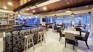 A modern bar area with a wooden ceiling, a bar counter with a patterned backlit design, and seating with a city view. - San Juan Hotel Boutique Pasto (San Juan de Pasto)