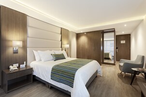 Una habitación de hotel moderna con una cama grande, lámparas de noche, una mesita de noche, un escritorio con una silla y un armario.