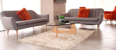 Una sala de estar moderna con dos sofás grises, una mesa de centro de vidrio y una alfombra de pelo alto blanca.