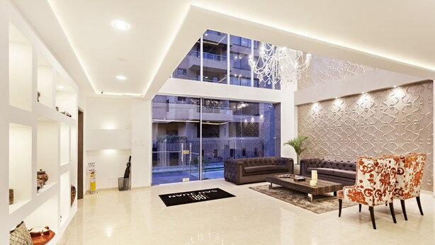 A modern living room with a sofa, chairs, a coffee table, and a large window offering a view of the building's exterior. - San Juan Hotel Boutique Pasto (San Juan de Pasto)