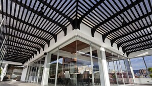 A modern building with a glass facade, a covered outdoor area with seating, and a view of the surrounding cityscape. - San Juan Hotel Boutique Pasto (San Juan de Pasto)