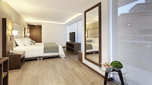A modern hotel room with a large bed, a TV, a mirror, and a window with a view of a building. - San Juan Hotel Boutique Pasto (San Juan de Pasto)