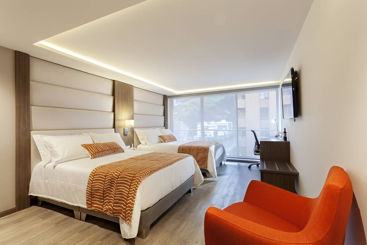 Ein modernes Hotelzimmer mit zwei Betten, einem Schreibtisch und hellem Blick auf die Stadt.