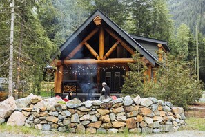 A log cabin with a stone foundation, wooden beams, and a chimney emitting smoke.