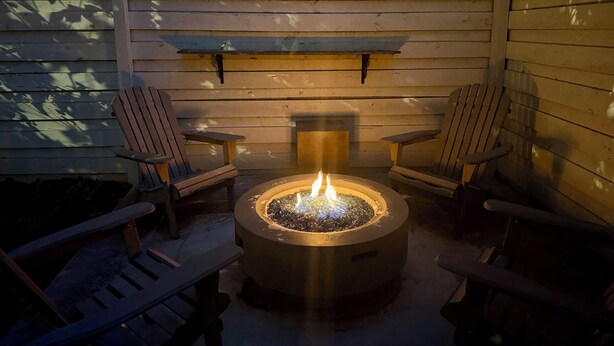 A fire pit with two Adirondack chairs around it, set against a wooden wall with a built-in bench above. - Studio Apartment with Office Space at Lake Guntersville - Scottsboro, AL (Scottsboro)