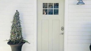 A white door with a small window, a potted plant, and a doormat. - Studio Apartment with Office Space at Lake Guntersville - Scottsboro, AL (Scottsboro)