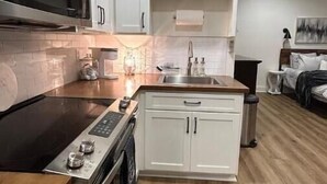 A modern kitchen with white cabinets, a stainless steel microwave, and a black induction cooktop. - Studio Apartment with Office Space at Lake Guntersville - Scottsboro, AL (Scottsboro)