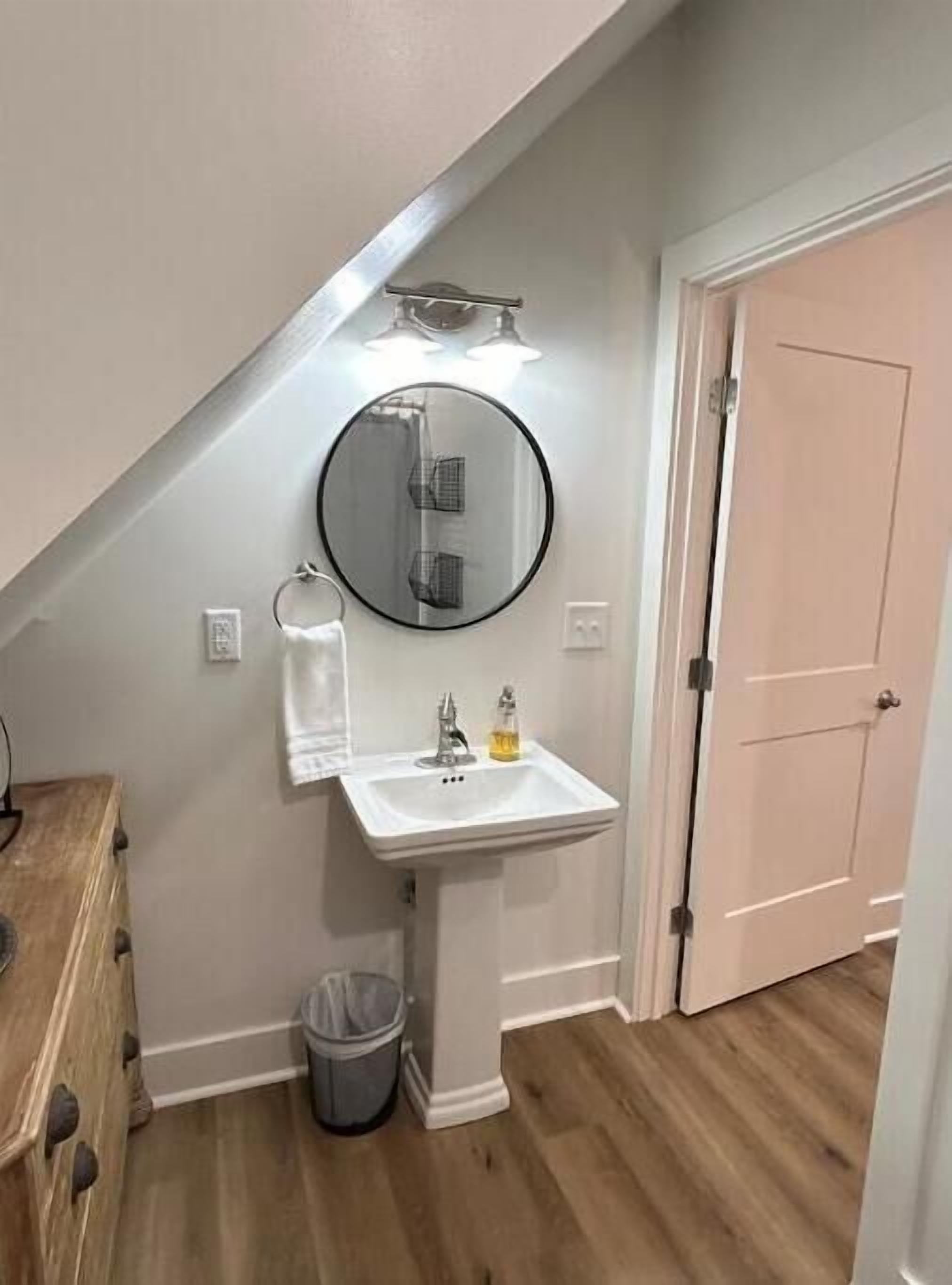 A bathroom with a white pedestal sink, a round mirror, and a towel rack.