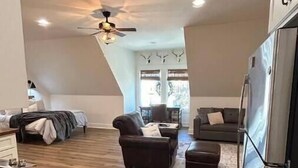A spacious living area with a high ceiling, a ceiling fan, and a large window providing natural light. - Studio Apartment with Office Space at Lake Guntersville - Scottsboro, AL (Scottsboro)