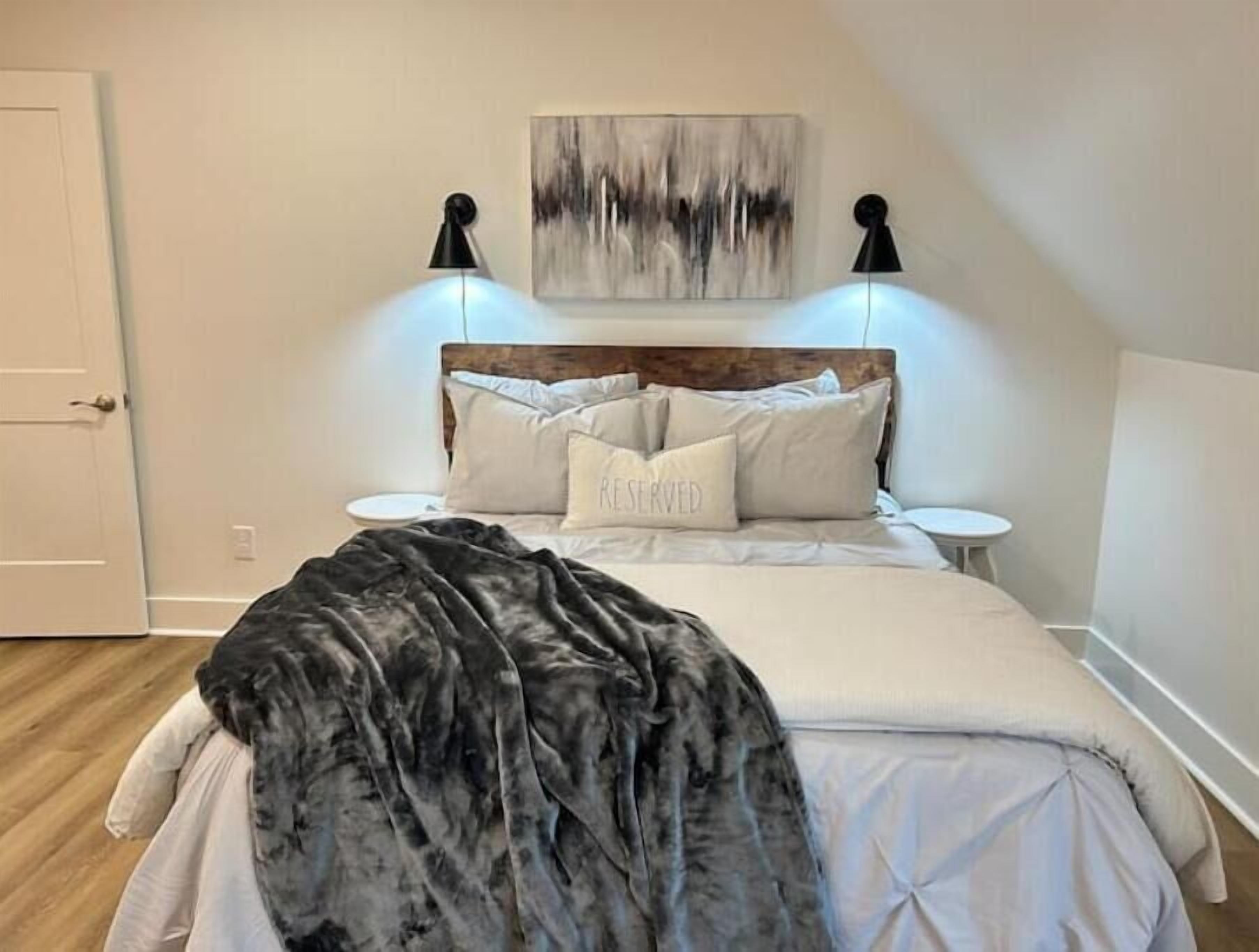 A bedroom with a bed, two bedside tables, a nightstand, a painting on the wall, and a door.