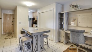 Una cocina moderna con una isla central, taburetes de bar, una silla de escritorio gris y una puerta blanca.