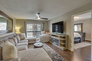 A living room with a sectional sofa, a round coffee table, a glass-top console table, a ceiling fan, and a large window with curtains.