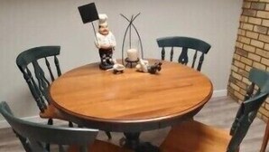 A round wooden dining table with six chairs, two wall clocks, and a small decorative figure. - Pam's Little Italy
 (Kelowna)