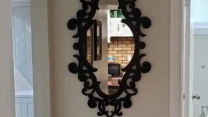 A hallway with a decorative black mirror on the wall, wooden flooring, and a door leading to another room. - Pam's Little Italy
 (Kelowna)