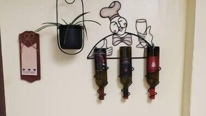 A wine rack with bottles, a small table with a box of wine glasses, and a trash can. - Pam's Little Italy
 (Kelowna)