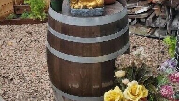A garden with a large wooden barrel, a golden Buddha statue, and various potted plants. - Pam's Little Italy
 (Kelowna)