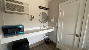 A compact bathroom with a white sink, a mirror, a towel rack, a trash bin, and a door. - Stone Creek Inn (Worth)