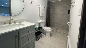 A modern bathroom with a large mirror, a sink with two faucets, a toilet, and a shower area with a curtain. - Stone Creek Inn (Worth)