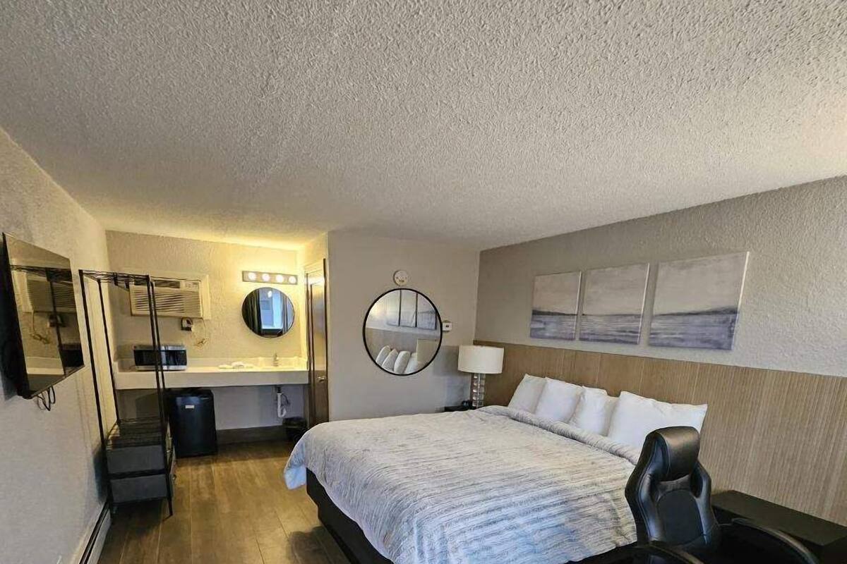 Une chambre d’hôtel comprenant un lit, un bureau, une chaise et une salle de bain avec un miroir et un lavabo.