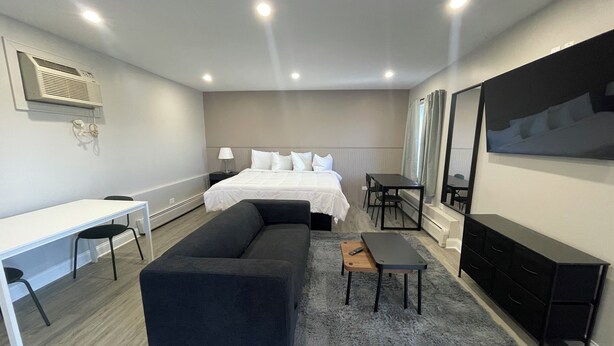 A modern hotel room with a bed, a desk, a sofa, a dining table, and a TV. - Stone Creek Inn (Worth)