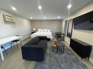 A modern hotel room with a bed, a desk, a sofa, a dining table, and a TV. - Stone Creek Inn (Worth)
