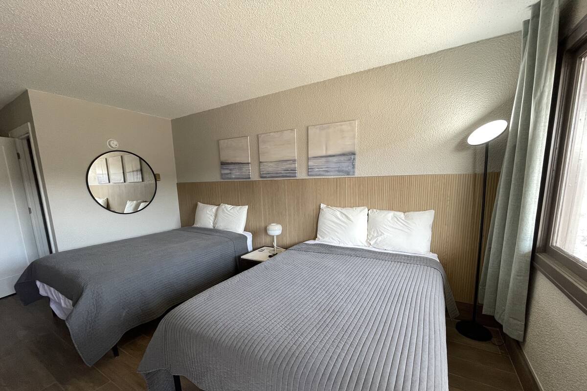 Une chambre d’hôtel avec deux lits, un miroir rond, une table de chevet, une lampe et des œuvres d’art accrochées au mur.