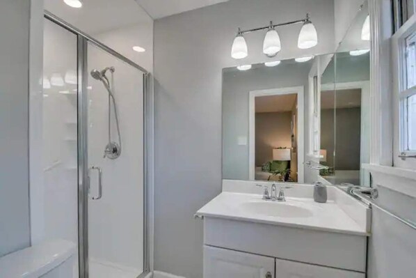 Une salle de bain moderne avec une douche à l’italienne en verre, un meuble-lavabo blanc avec un miroir et un éclairage encastré.