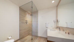 Un bany modern amb dutxa separada per una mampara de vidre, un lavabo i un moble de tocador amb mirall.