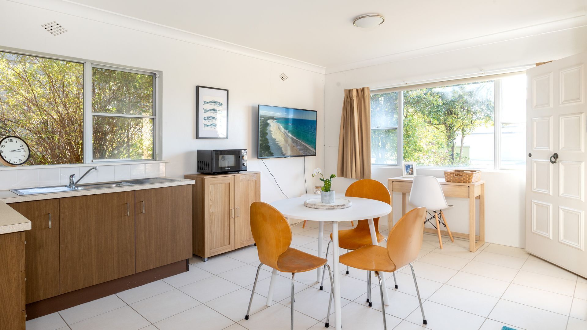 A modern kitchen with a dining area, wooden cabinets, a sink, and a large window with a view of trees.