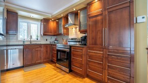 A modern kitchen with wooden cabinets, stainless steel appliances, and a large window. - Hôtel à la maison - Chalet Lola (St-Tite)