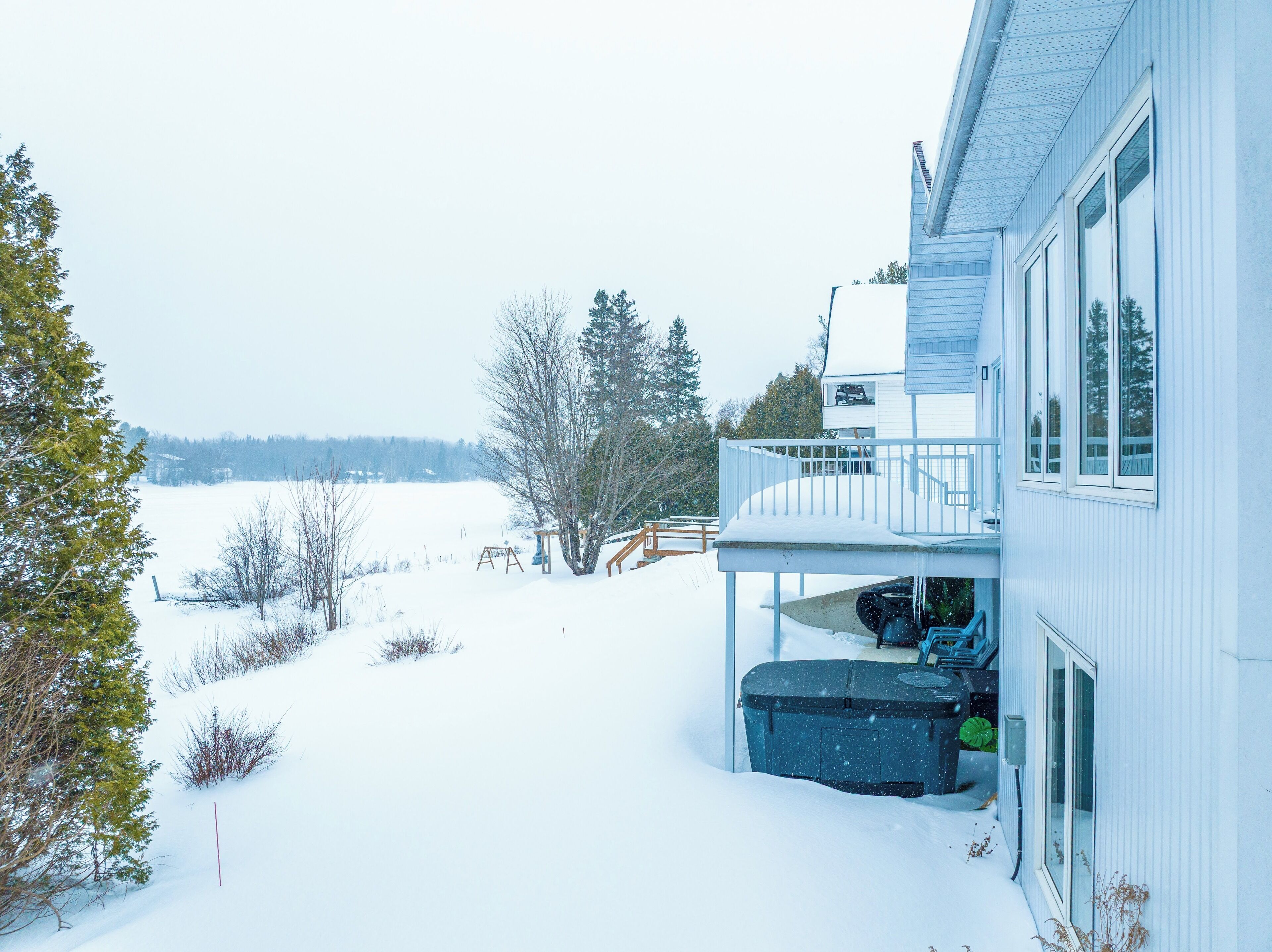 A snow-covered landscape with a house featuring a balcony and a covered outdoor area.