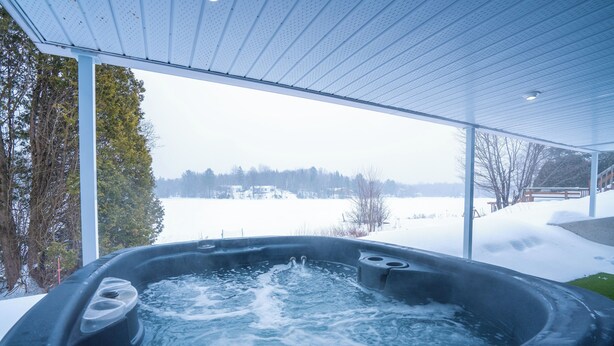 A hot tub with a view of a snowy landscape through large windows. - Hôtel à la maison - Chalet Lola (St-Tite)