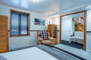 A bedroom with a bed, a chair, a window with blinds, a cabinet, and a staircase. - Hôtel à la maison - Chalet Lola (St-Tite)