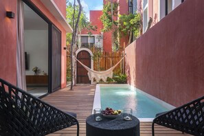 A poolside area with a hammock, a table with fruit and glasses, and a view of a building with red walls and a wooden deck.