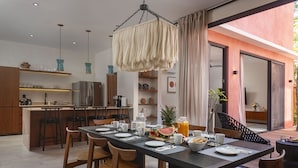 A modern kitchen with a central island, wooden chairs, and a dining table set for six. - Casa Ananta (Tulum)