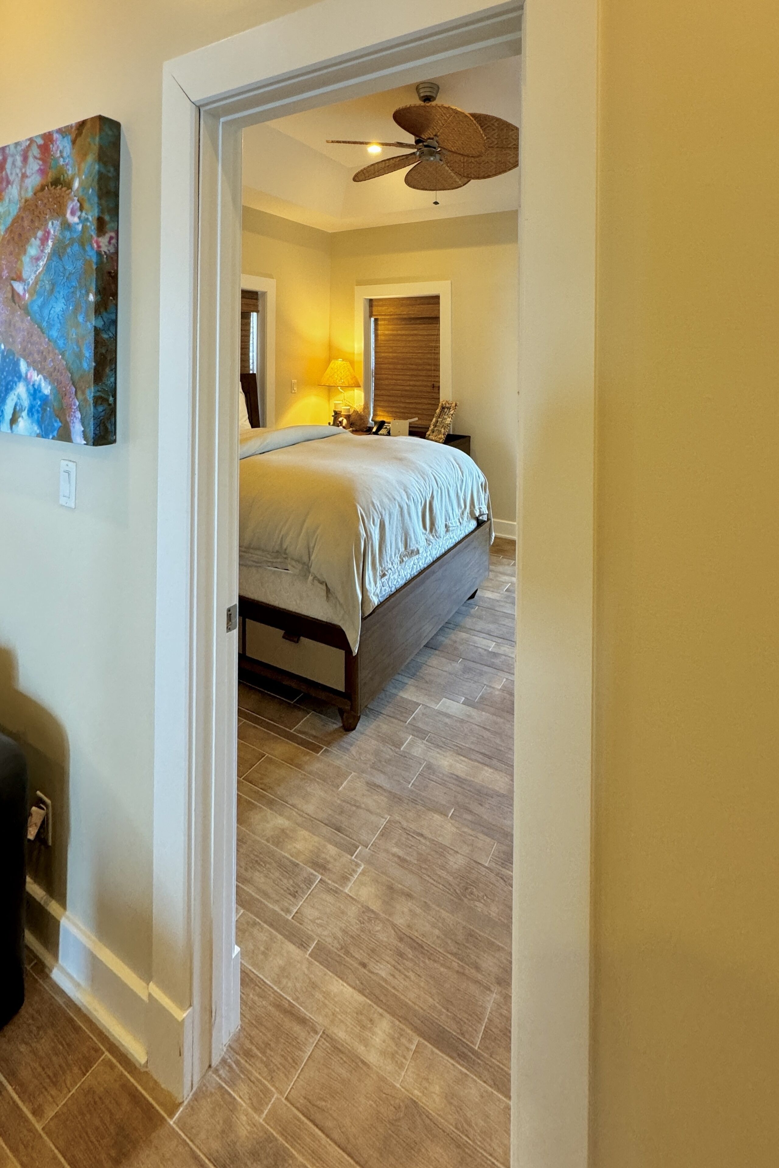 Une chambre à coucher avec un lit, un ventilateur de plafond et une porte donnant sur une autre pièce.