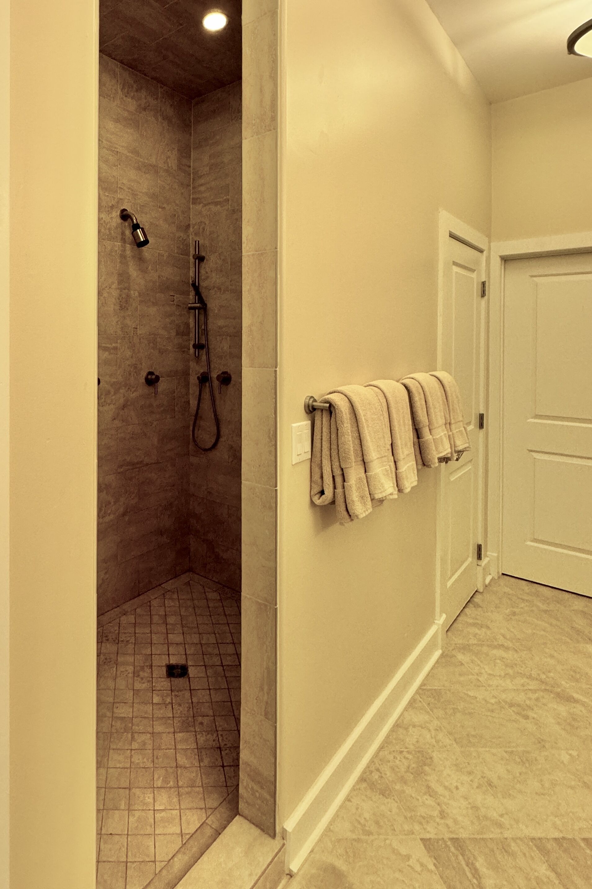 A bathroom with a walk-in shower, tiled floor, and a towel rack with towels.
