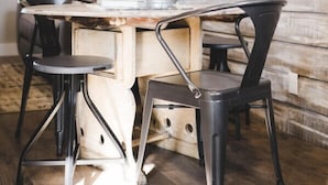 A dining area with a rustic wooden wall, a wooden table, and black chairs.