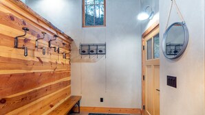 Un banco de madera, una ventana pequeña, un espejo y una puerta en una habitación con pared de madera.
