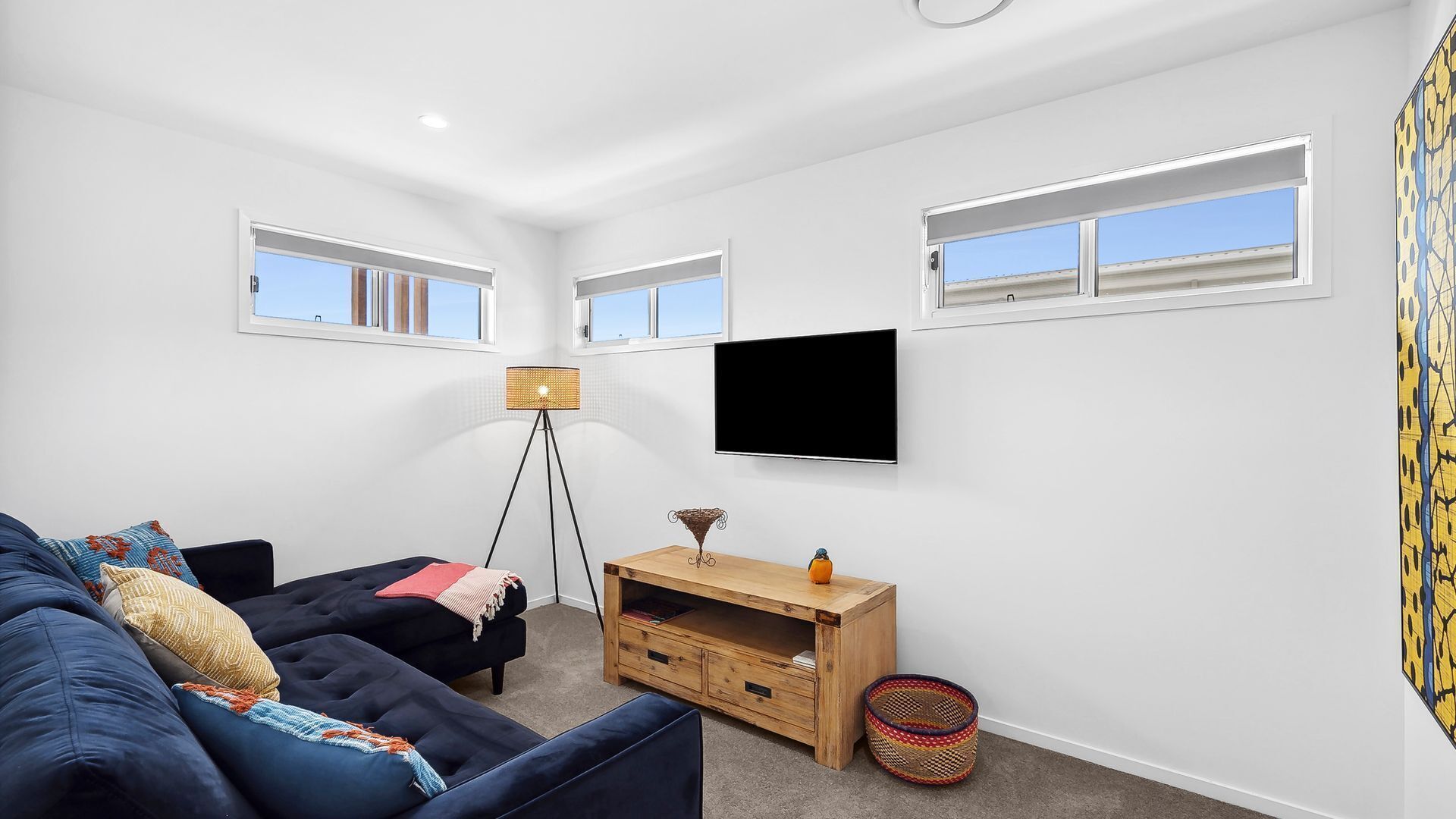 A modern living room with a dark blue sofa, a small wooden TV stand, a floor lamp, and a large window with blinds.
