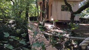 Una cabaña de madera rodeada de árboles, accesible por un camino de madera.