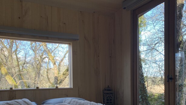 Una habitación de cabaña de madera con una cama, almohadas, una ventana y vistas a árboles.