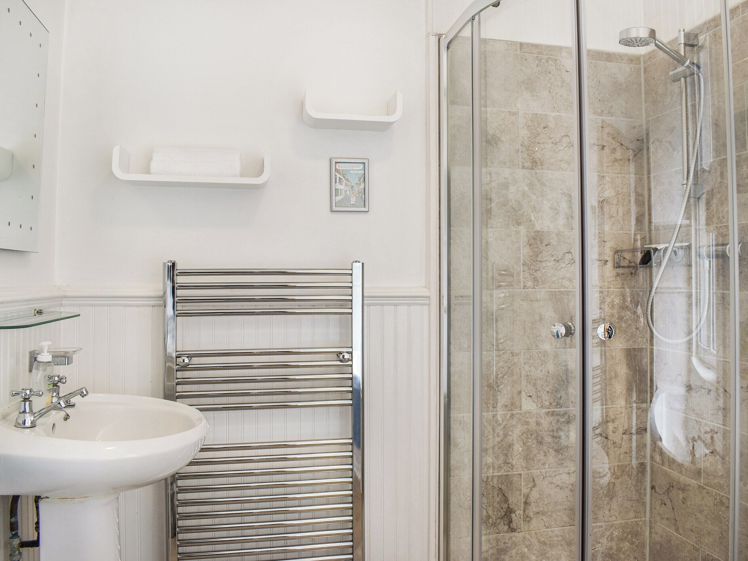 A bathroom with a glass-enclosed shower, a white sink, and a towel rack.